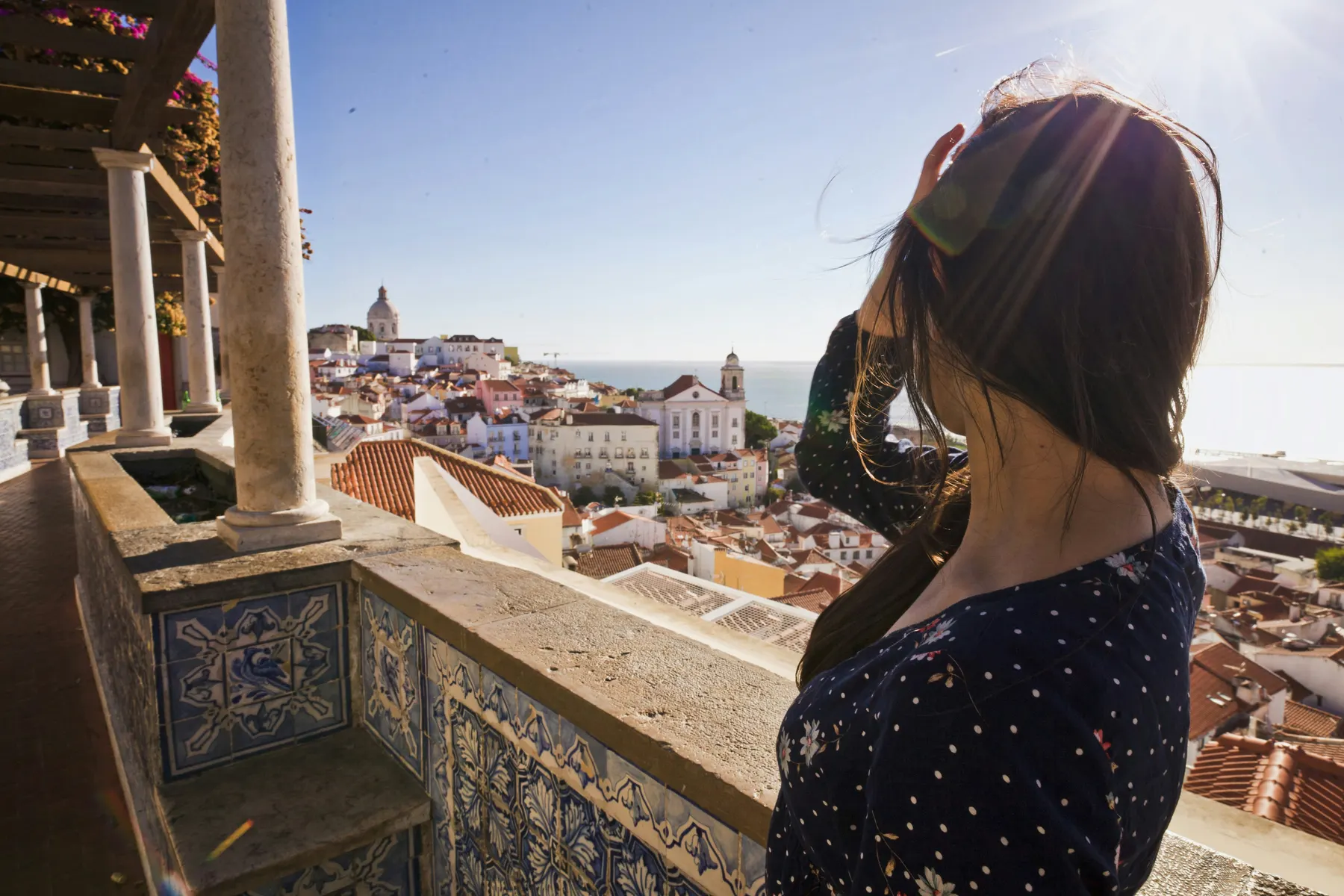 Frau blickt von einem Balkon über die Dächer von Lissabon